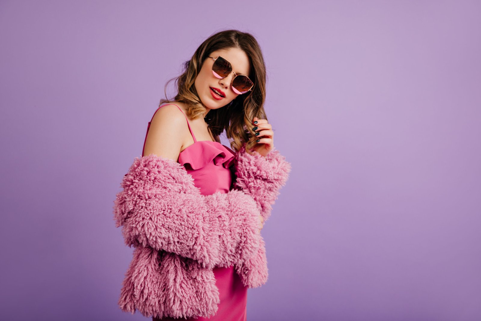 Blithesome girl with brown hair standing on violet background. Enthusiastic woman in pink eco jacket looking to camera.